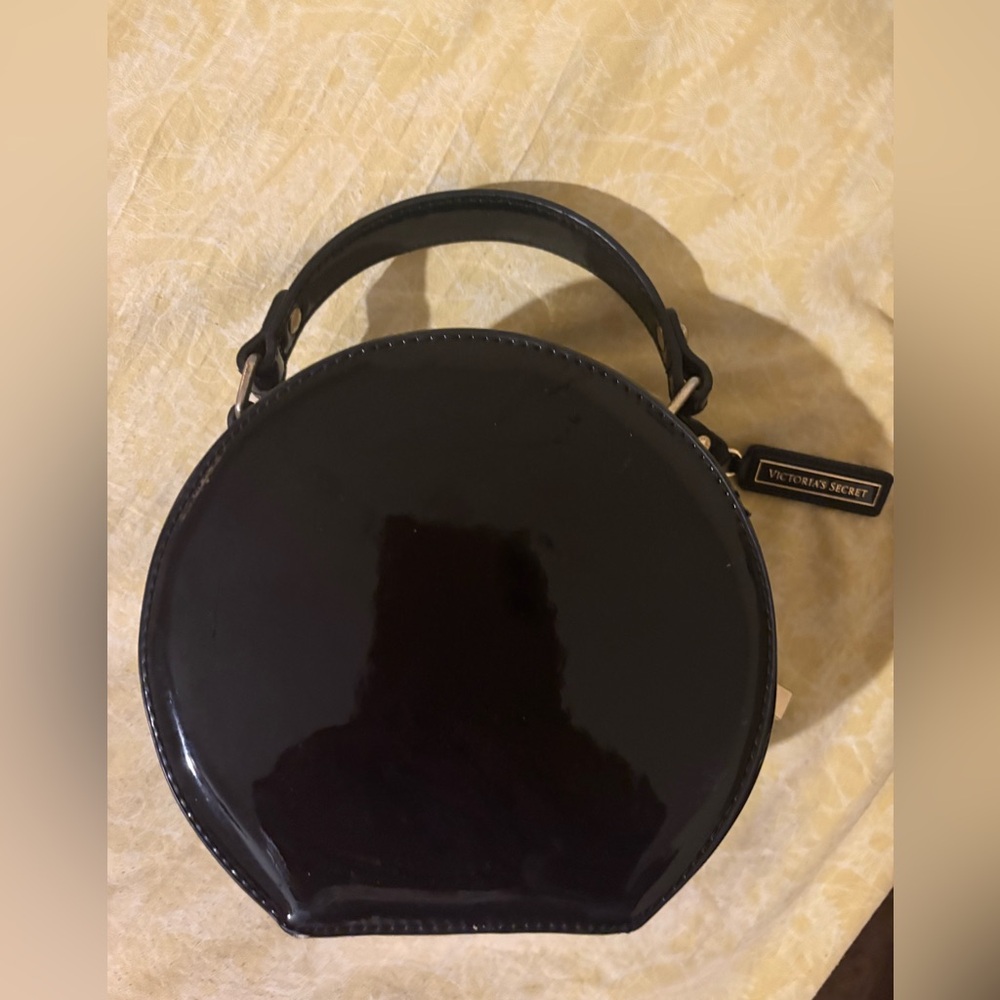 This is a black, round, patent leather-like handbag from Victoria's Secret.